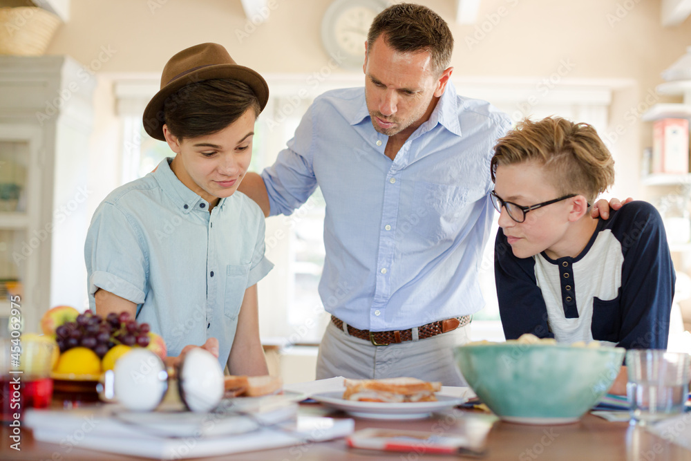 Teenage boys with father using laptop in dining room Teenage boys with father using laptop in dining room
