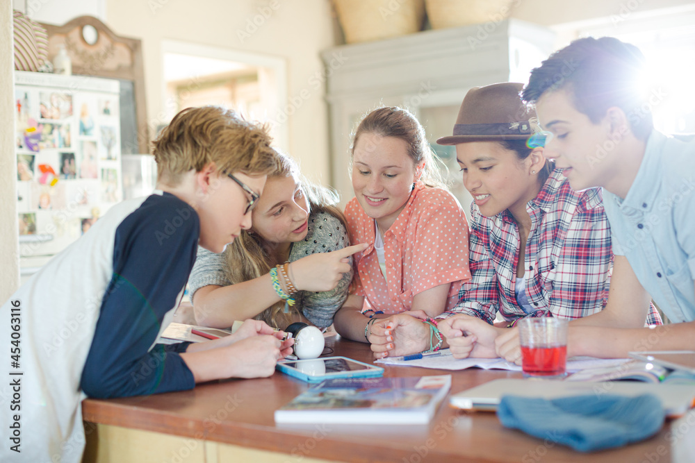 Group of teenagers using together digital tablet at table in kitchen Group of teenagers using together digital tablet at table in kitchen