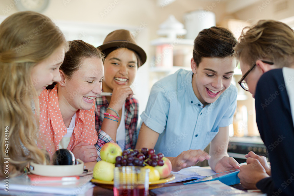 Group of teenagers using together digital tablet at table in kitchen Group of teenagers using together digital tablet at table in kitchen