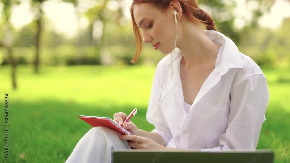 Girl sitting in the grass writing something in notes and working with a laptop Girl sitting in the grass writing something in notes and working with a laptop