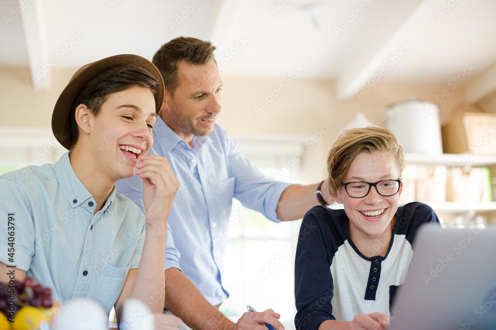 Fototapeta premium Teenage boys with father using laptop in dining room