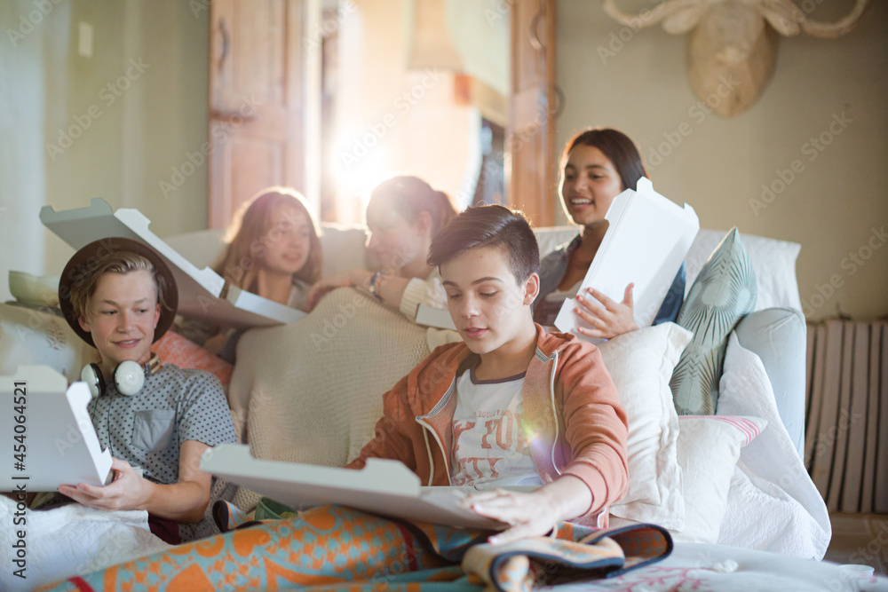Fototapeta premium Group of teenagers opening pizza boxes on sofa in living room