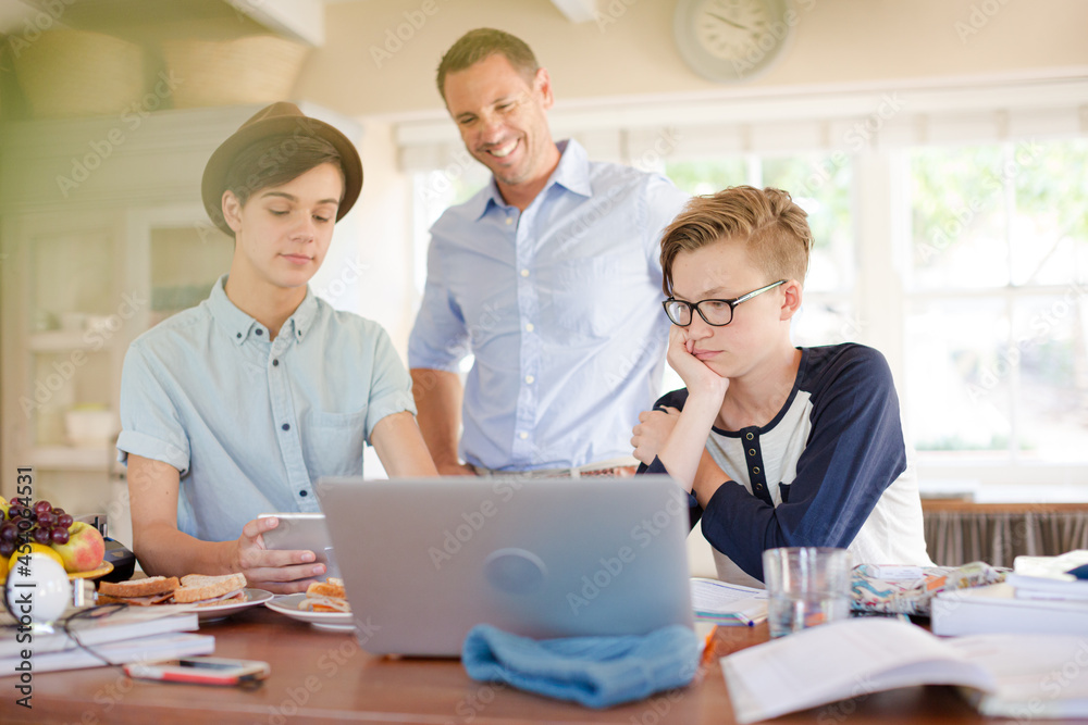 Teenage boys with father using laptop in dining room Teenage boys with father using laptop in dining room