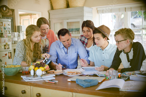Teenagers with mid adult man sitting at table in dining room
