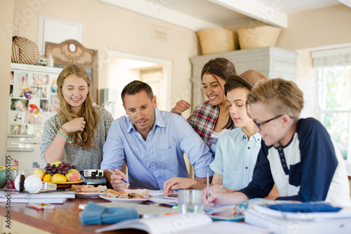 Teenagers with mid adult man sitting at table in dining room