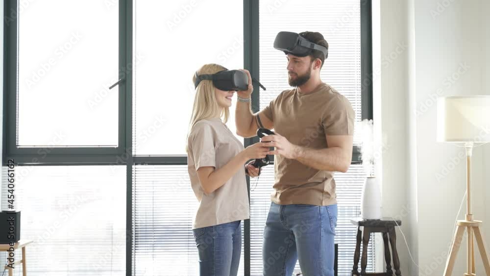 Guy helps a girl wear VR glasses. Positive beautiful caucasian couple playing video games in virtual reality glasses. Guy helps a girl wear VR glasses. Positive beautiful caucasian couple playing video games in virtual reality glasses.
