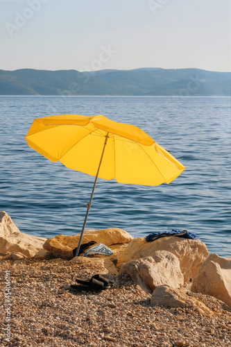 Yellow beach umbrella on summer coast. Sea beach with sun umbrella is waiting for tourists on Sunset. Happy summer resort concept. Vertical view.