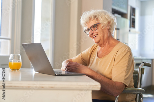 Senior woman in a wheelchair at the computer is happy about the video call