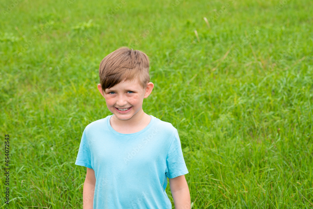 European child on the field, smiling little boy in a blue T-shirt on a background of grass European child on the field, smiling little boy in a blue T-shirt on a background of grass