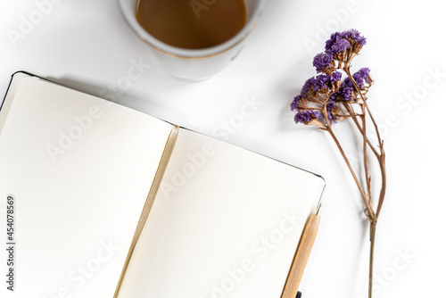 Writing pad with a cup of coffee, pen and flowers. Table flat lay with space for a caption. Clean and neat composition.