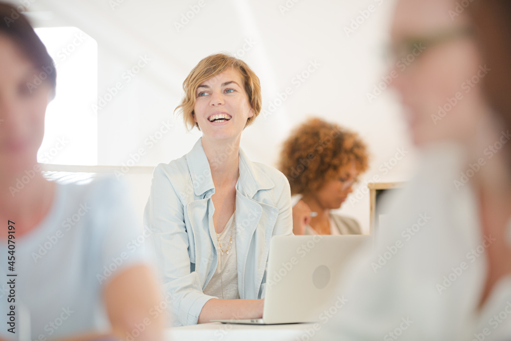 Fototapeta premium Portrait woman sitting at desk, using laptop smiling in office, colleagues
