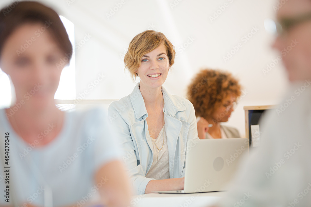 Portrait woman sitting at desk, using laptop smiling in office, colleagues Portrait woman sitting at desk, using laptop smiling in office, colleagues