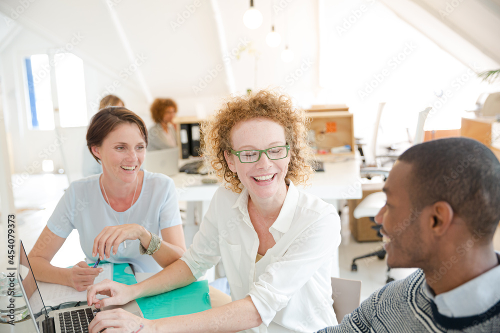 Office workers talking over laptop at desk Office workers talking over laptop at desk