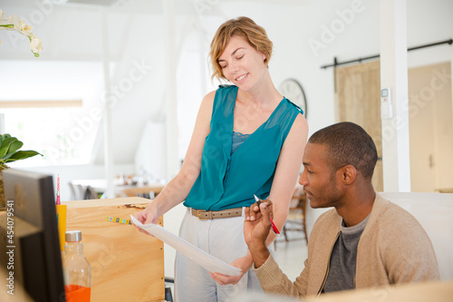 Woman and man looking at documents, talking and smiling in office © KOTO