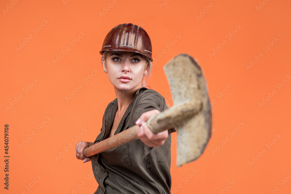woman worker in protective helmet and boilersuit hold shovel on orange background, industry woman worker in protective helmet and boilersuit hold shovel on orange background, industry