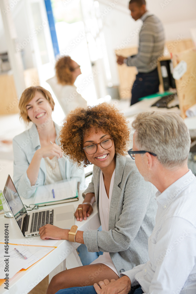 Obraz premium Three office workers talking at desk with laptop