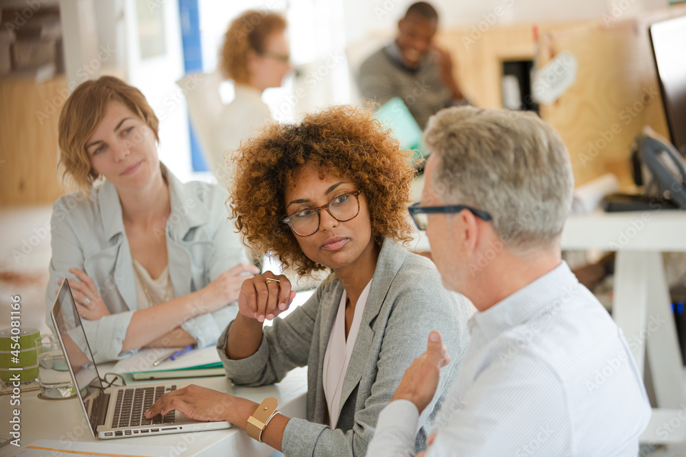 Fototapeta premium Three office workers talking at desk with laptop