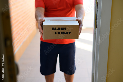Unrecognizable man delivering a cardboard package marked black friday to the door of a house.