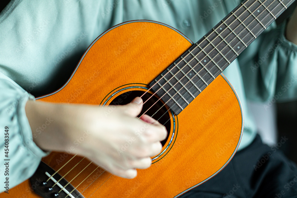 Fototapeta premium Woman strumming strings of wooden solid acoustic guitar.