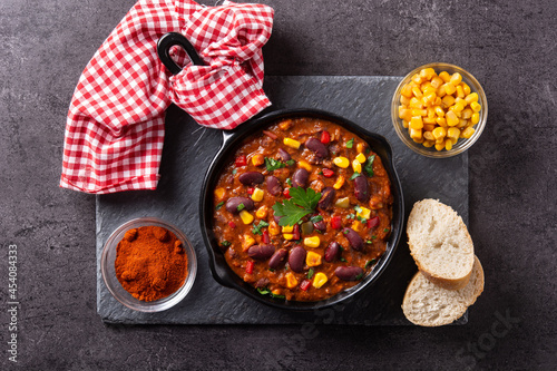 Traditional mexican tex mex chili con carne in iron pan on black background