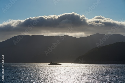 Schiff auf glitzerndem Meer vor Insel unter Wolken, Porto Ferraio, Elba, Italien