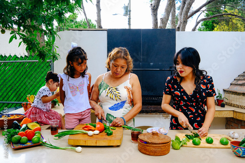 Girl looking at aunt learning chopping vegetables from grandmother while preparing salsa in backyard