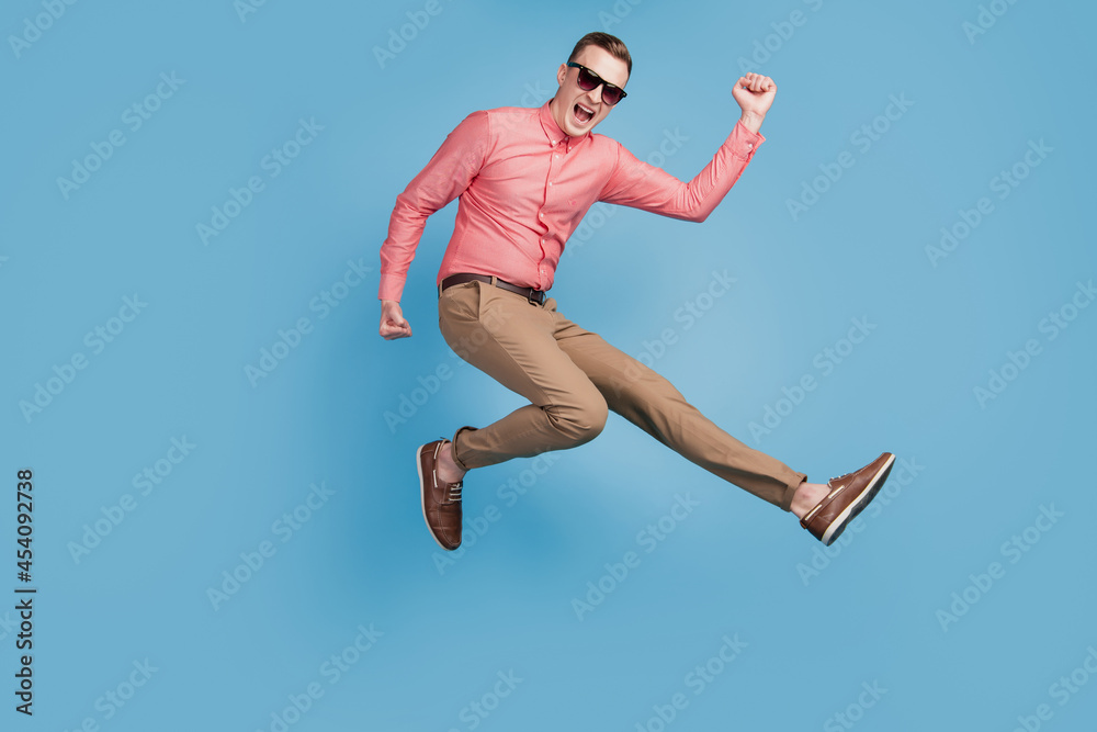 Portrait of astonished excited cool guy jump run winner concept on blue background