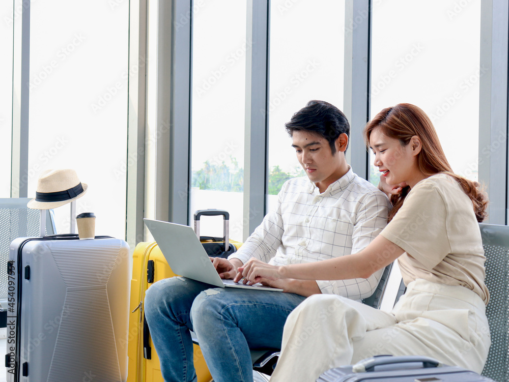 Asian young traveler lover couple siting on terminal chair seat with luggage suitcase, using laptop computer together, talking having and having fun times, happy friend traveling on vacation. Asian young traveler lover couple siting on terminal chair seat with luggage suitcase, using laptop computer together, talking having and having fun times, happy friend traveling on vacation.