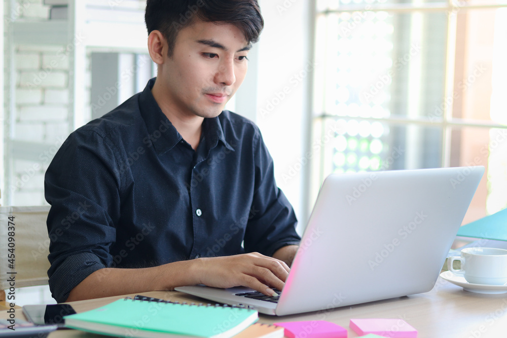 Asian young handsome businessman in black shirt typing on keyboard laptop computer on working desk at nice modern office. Asian young handsome businessman in black shirt typing on keyboard laptop computer on working desk at nice modern office.