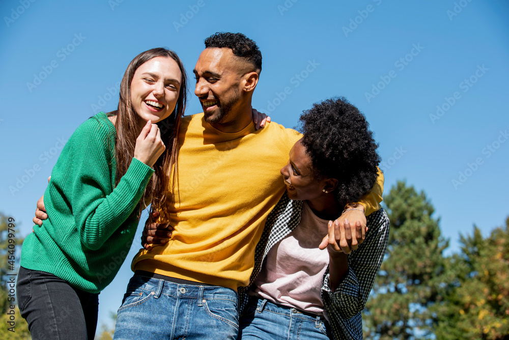 Smiling young friends standing with arm around in public park Smiling young friends standing with arm around in public park