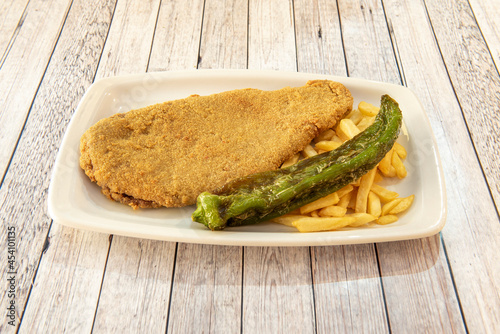 Popular dish from northwestern Spain. Cachopo, beef fillet with ham and cheese and battered with flour, egg and breadcrumbs with a guanicion of fried potatoes and fried green pepper photo