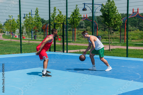 Multiethnic streetball players training with basketball ball on playground
