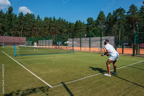 African american sportsman playing tennis with friend on court
