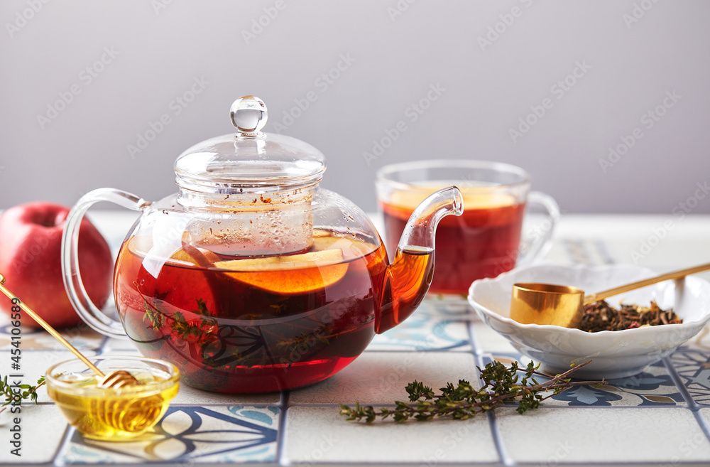 Fruit tea with apples and thyme in glass teapot and cup on table made of colored tiles Fruit tea with apples and thyme in glass teapot and cup on table made of colored tiles