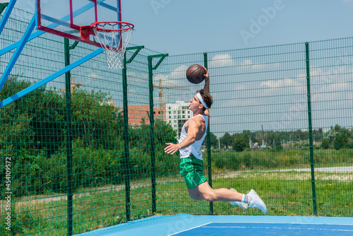 Side view of sportsman jumping under hoop while playing streetball
