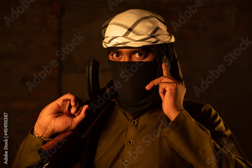 Terrorist or gangster with face cover blackmailing or asking for ransom over mobile phone call and warning by showing gun. photo