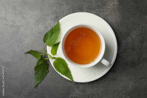 Cup of aromatic nettle tea and green leaves on grey table, top view