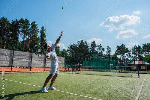 Young sportsman holding racket near ball while playing tennis with african american friend © LIGHTFIELD STUDIOS