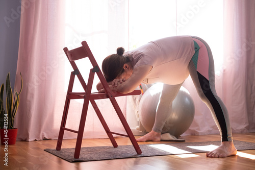 Pregnant woman doing inversion Standing Intense Spread Leg Prasarita Padottanasana yoga pose at home photo