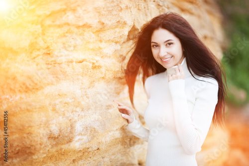 Young fashion woman with long hair in white dress relax near beautiful stones. Happy autumn beach lifestyle