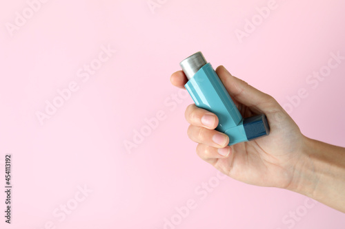 Female hand holds asthma inhaler on pink background photo