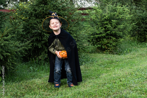 a child in a wizard's fancy dress holds an orange jack-o-lantern pumpkin in his hands. Happy Halloween. the boy in the wizard's hat, celebrating All Saints ' Day. trick-or-treat