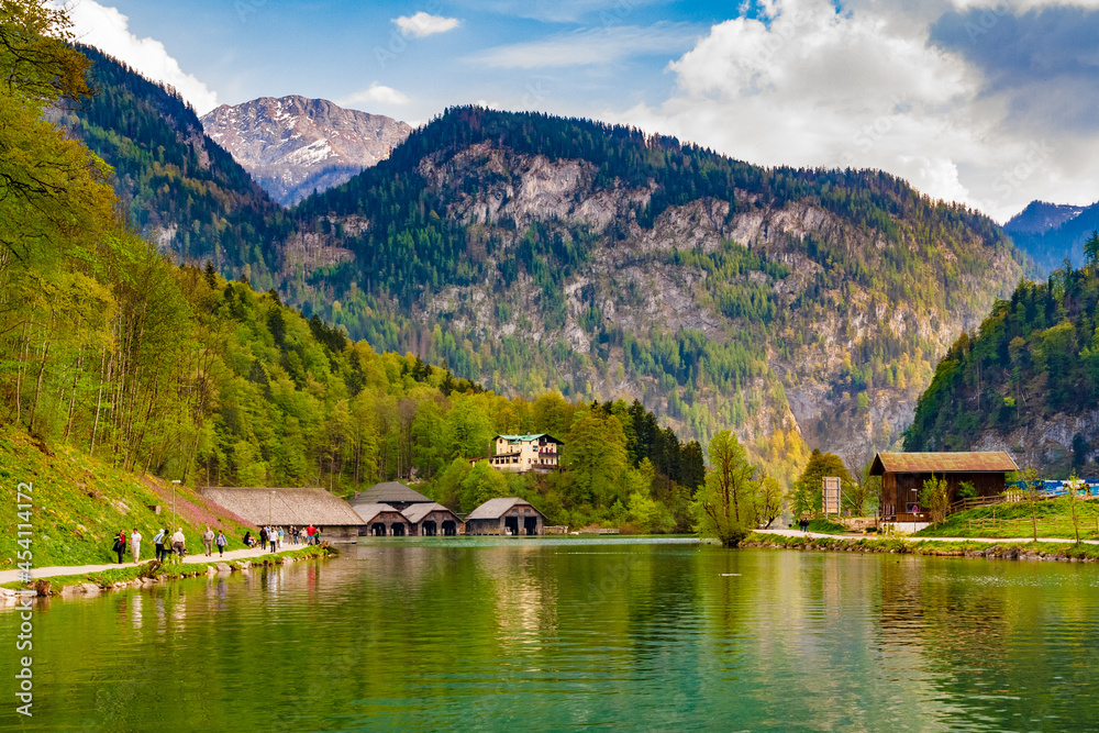 Picturesque landscape view of the northern end of the Königssee lake surrounded by mountains in Bavaria, Germany. In front is a row of boathouses and in the background are the alps.