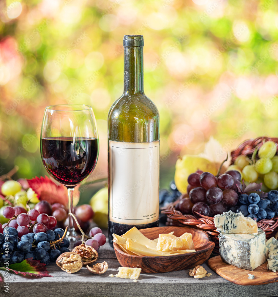 Grapes, bottle of wine and different cheeses on country wooden table and blurred colorful autumn background. Variety of products as the symbol of autumn abundance and prosperity. Grapes, bottle of wine and different cheeses on country wooden table and blurred colorful autumn background. Variety of products as the symbol of autumn abundance and prosperity.