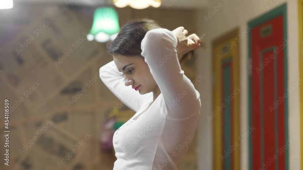 Side view of a young woman, she collects her hair in a ponytail. A beautiful young woman combs her hair in front of the mirror.