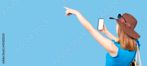 Back view photo of a beautiful woman in summer time wearing hat with sunglasses above holding the smartphone and pointing with the raised hand and index finger.