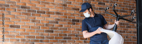 workman in cap and medical mask holding office chair near brick wall, banner © LIGHTFIELD STUDIOS