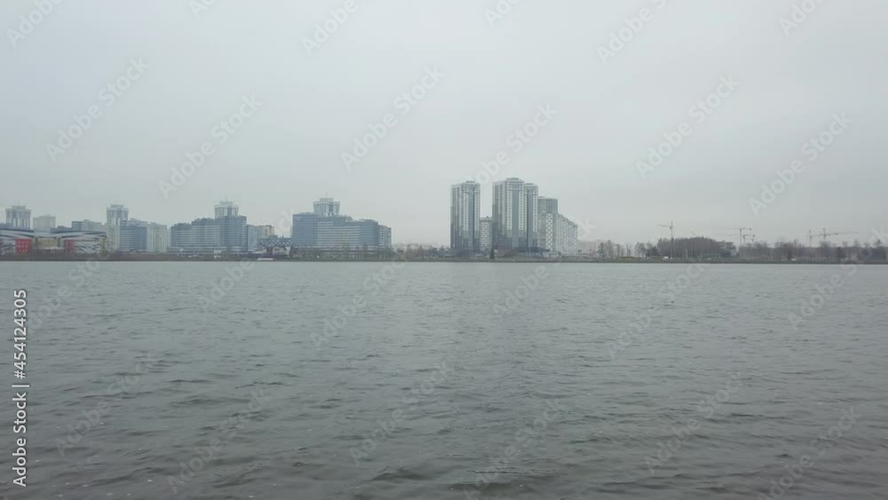 Drone flying over cold autumn lake. The big city in fog on background. Various buildings near beautiful still lake shore. Urban concept. Drone flying over cold autumn lake. The big city in fog on background. Various buildings near beautiful still lake shore. Urban concept.
