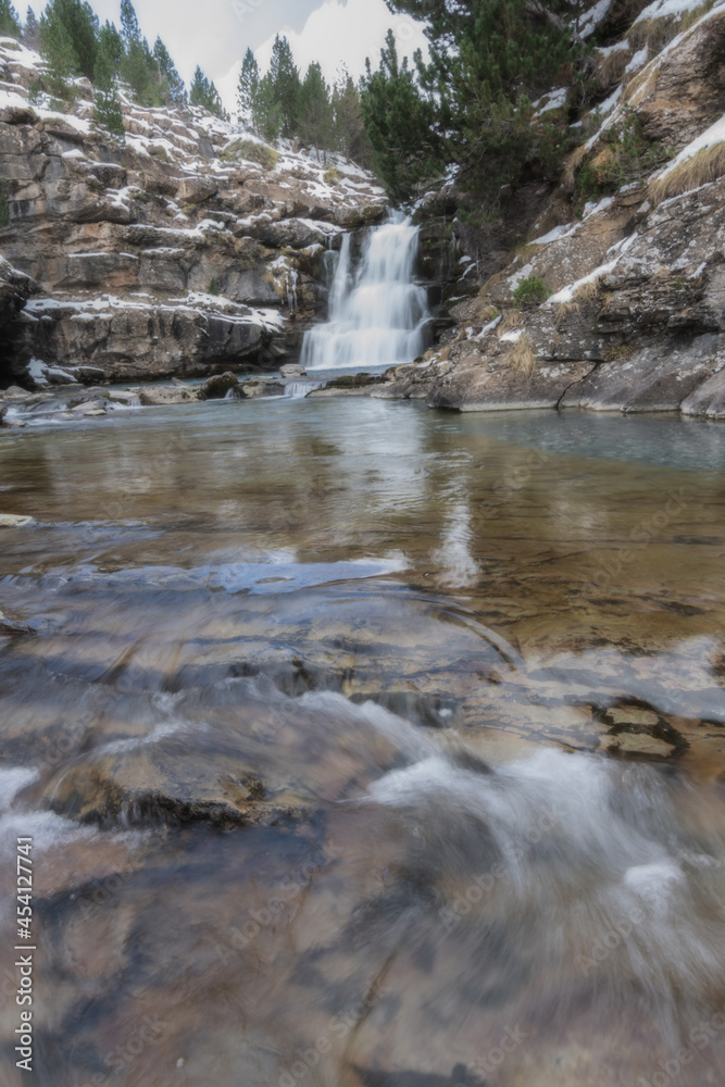 River waterfall in a valley in a mountain river landscape in snowy winter, with trees in Ordesa Valley, Pyrenees, national park, Spain.
Vertical view River waterfall in a valley in a mountain river landscape in snowy winter, with trees in Ordesa Valley, Pyrenees, national park, Spain.
Vertical view
