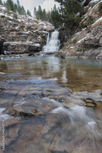 River waterfall in a valley in a mountain river landscape in snowy winter  with trees in Ordesa Valley  Pyrenees  national park  Spain. Vertical view